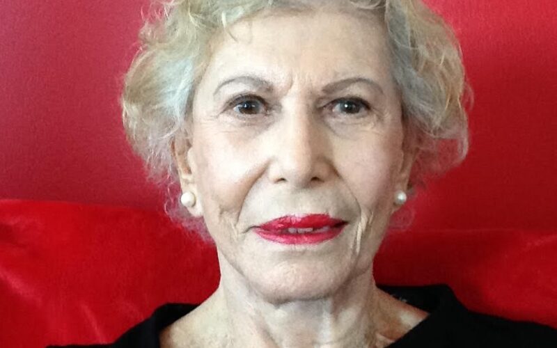 Reinventing in your 80s: picture of Stephanie Schwartz, a silver-haired woman wearing a black top. There is a red background in the picture