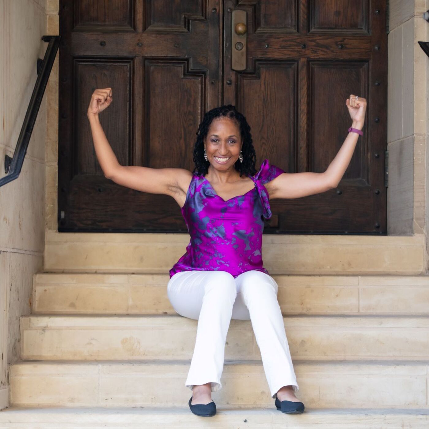 Picture of Wendy Battles sitting on the steps outside of a building. She is flexing both arms to make muscles. Her motto is reinvent yourself no matter your age, it's never too late.