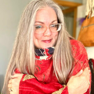 Grey Hair looks great on Tangled Silver magazine publisher Robin Salls. A picture of her in a red top hugging herself as she looks into the camera