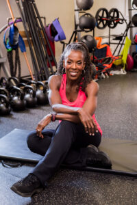 Picture of Kathy Murray sitting on a gym mat in workout clothes. Kathy knows a lot about reinventing midlife, having done it multiple times.