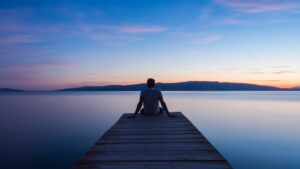 Reinventing yourself starts with getting quiet and still. Picture of person sitting at the end of a pier at sunset.