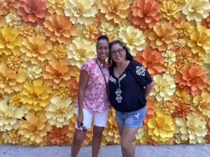 Midlife friendships are the best! Picture of Wendy Battles and Wendy Hutchinson meeting for the first time in San Antonio Texas. They are pictured in front of a wall of orange and yellow flowers.