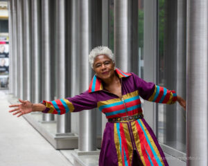 Reinvention looks good on Carolyn Doelling. This 74-year old is wearing a multicolored dress leaning out her right arm and smiling at the camera.