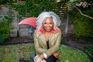 Midlife entrepreeneur Angel Cornelius is smiling at the camera, sitting outside in a garden