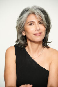 Aging powerfully. That's what Laureen is doing at 58. Pictured here with silver hair and wearing a black dress, smiling into the camera with confidence